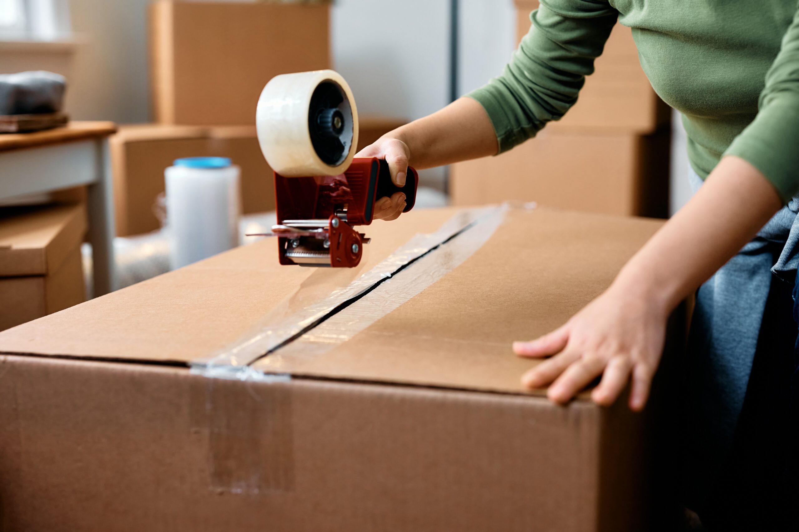 Person sealing a shipping box with packing tape for trade show exhibit transportation and material handling.